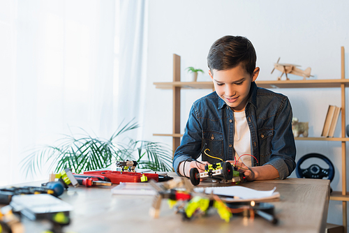 preteen kid assembling robotics model near mechanical details on blurred foreground