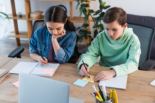 high angle view of preteen friends doing homework near laptop at home