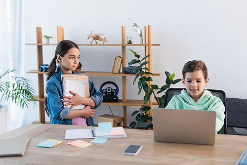 girl with notebooks looking at boy using laptop at home