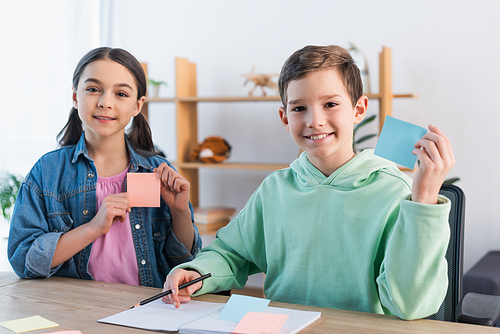 smiling kids looking at camera and showing blank sticky notes