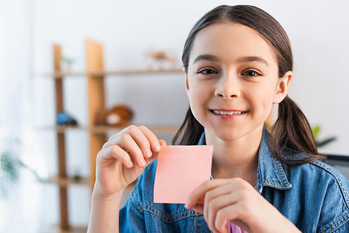 happy brunette girl looking at camera while holding blank sticky note