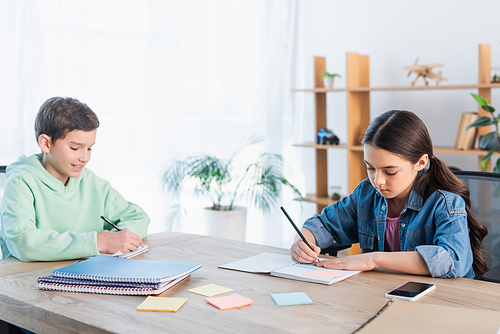 smiling boy and concentrated girl writing in notebooks near empty sticky notes