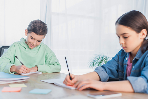 preteen kids writing in notebooks while doing homework on blurred foreground