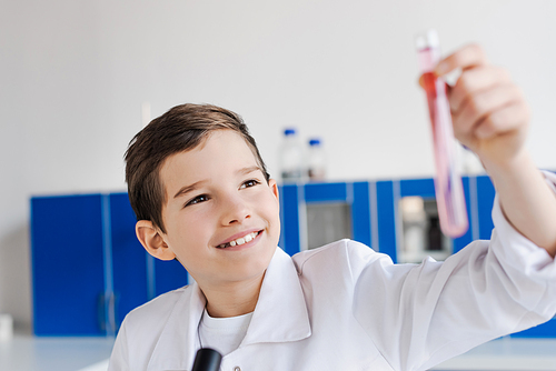 cheerful preteen boy looking at blurred test tube while making chemical experiment in lab