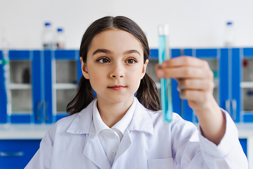 brunette girl in white coat holding blurred test tube in lab