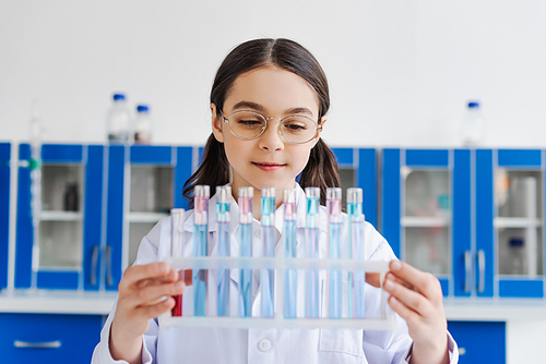 smiling preteen girl in eyeglasses holding test tubes in laboratory
