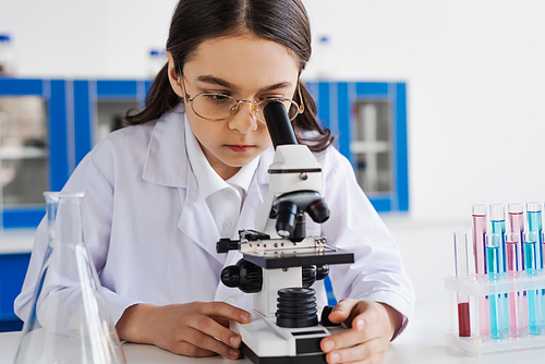 brunette girl in white coat and eyeglasses using microscope in lab