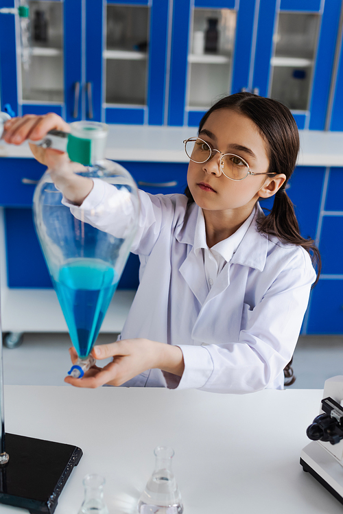 girl in eyeglasses and white coat holding flask with blue liquid in lab