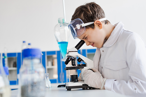 side view of boy in white coat looking into microscope on blurred foreground