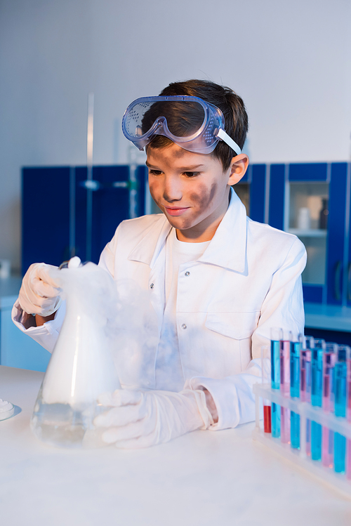 preteen boy with dirty face holding steaming flask while making chemical experiment in lab