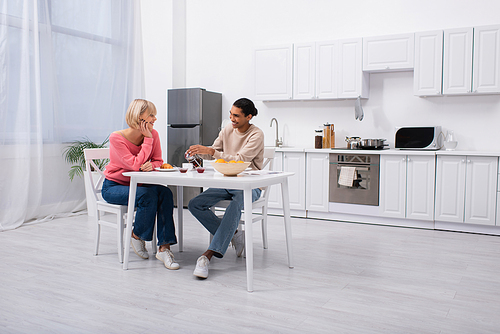 positive african american man pouring tea near blonde girlfriend