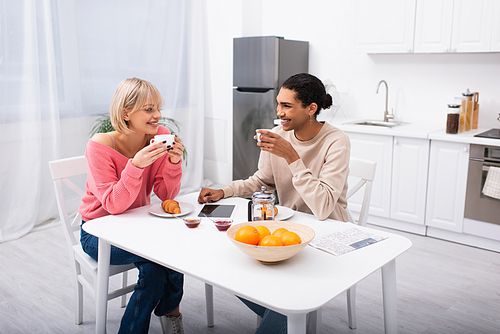 happy multiethnic couple drinking tea during breakfast and looking at each other