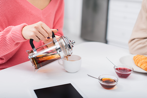 cropped view of woman pouring tea near digital tablet with blank screen