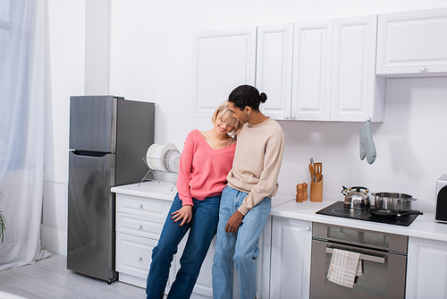 happy multiethnic couple hugging in modern kitchen