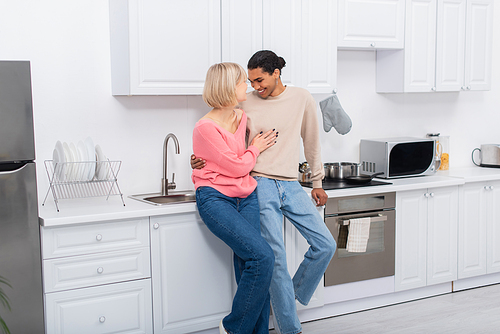 happy multiethnic couple hugging each other in modern kitchen