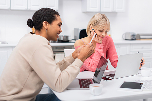 happy african american man using smartphone near smiling girlfriend working from home on laptop