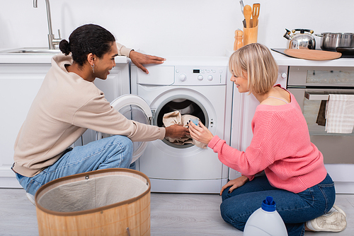 happy interracial couple putting clothes in washing machine