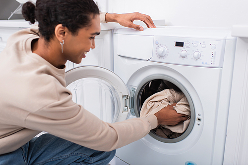 happy african american man putting laundry in washing machine