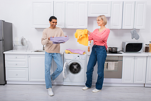 happy interracial couple holding clean and colorful clothes