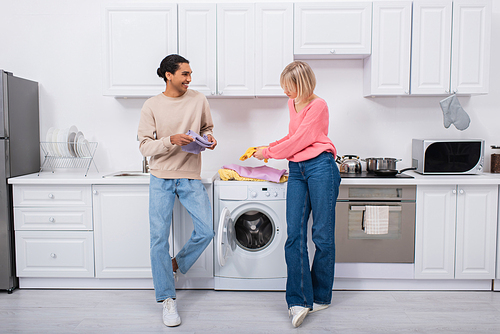 cheerful interracial couple holding clean and colorful clothes