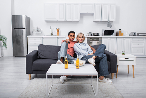 african american man holding remote controller and clicking channels near young girlfriend in living room