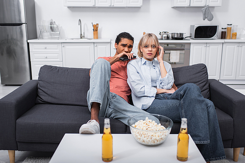 young multiethnic couple watching scary movie in living room