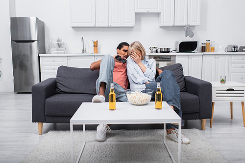 young emotional and interracial couple watching scary movie in living room