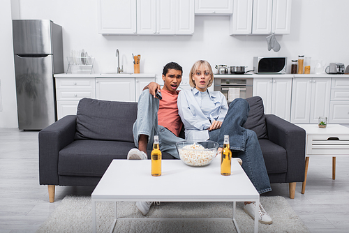 young shocked interracial couple watching scary movie in living room