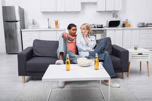 young interracial couple looking at each other while watching movie in living room