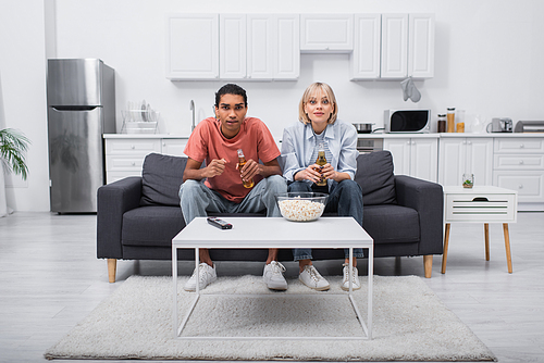 young multiethnic couple cheering while watching sport match in living room