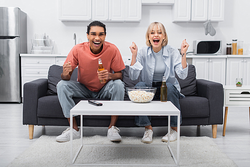 happy multiethnic couple cheering while watching sport match in living room