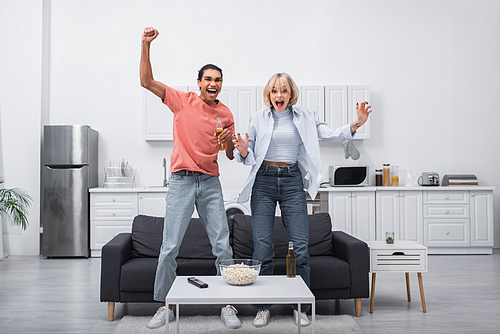 excited multiethnic couple jumping while watching sport match in living room