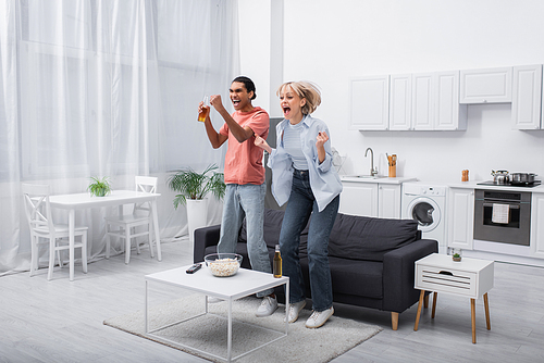 excited interracial couple jumping while watching sport match in living room