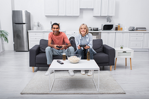 KYIV, UKRAINE - DECEMBER 6, 2021: excited multiethnic couple playing video game in living room