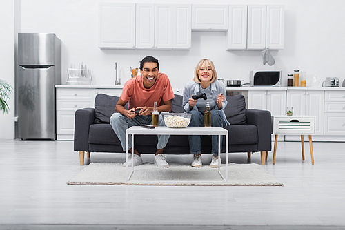 KYIV, UKRAINE - DECEMBER 6, 2021: happy multiethnic couple playing video game in living room