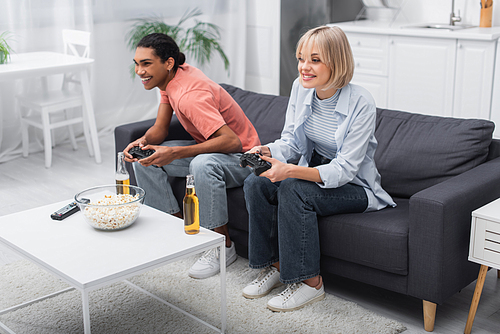 KYIV, UKRAINE - DECEMBER 6, 2021: happy multiethnic couple holding joysticks and playing video game