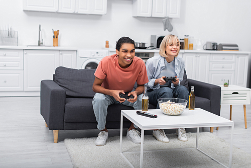 KYIV, UKRAINE - DECEMBER 6, 2021: cheerful multiethnic couple holding joysticks and playing video game