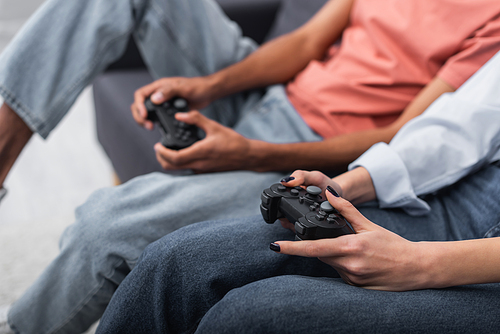 KYIV, UKRAINE - DECEMBER 6, 2021: partial view of multiethnic couple holding joysticks and playing video game