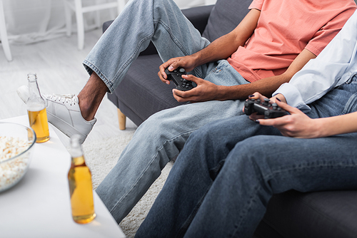 KYIV, UKRAINE - DECEMBER 6, 2021: partial view of multiethnic couple playing video game near bottles of beer