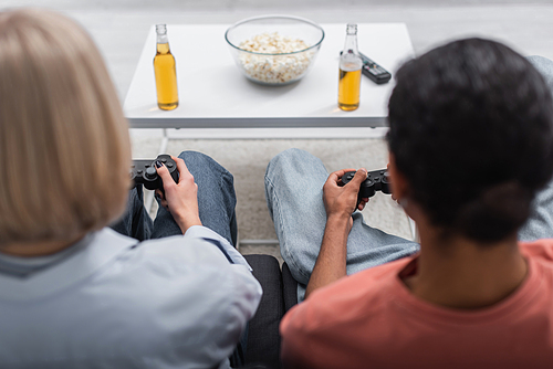 KYIV, UKRAINE - DECEMBER 6, 2021: back view of multiethnic couple holding joysticks and playing video game