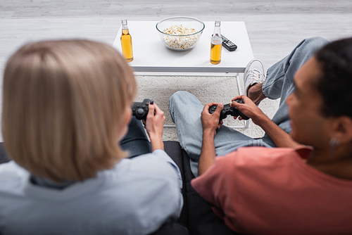 KYIV, UKRAINE - DECEMBER 6, 2021: popcorn and beer near multiethnic couple playing video game