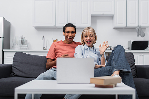 cheerful african american man near happy girlfriend waving hand during video call on laptop