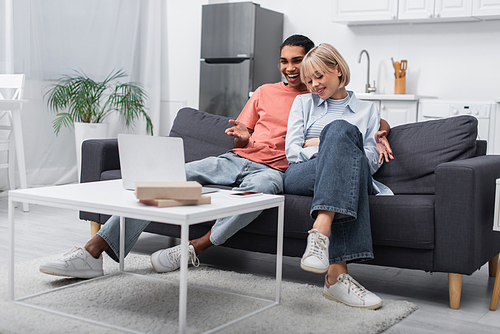 cheerful multiethnic couple smiling while watching movie on laptop