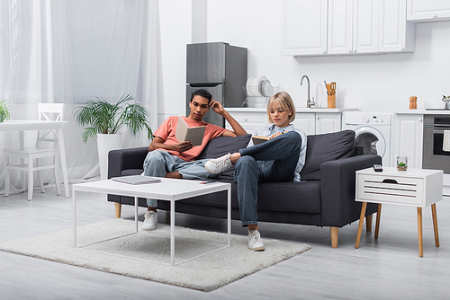 young interracial couple reading books near gadgets on coffee table