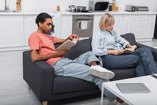 young african american man and blonde woman reading books near devices on coffee table