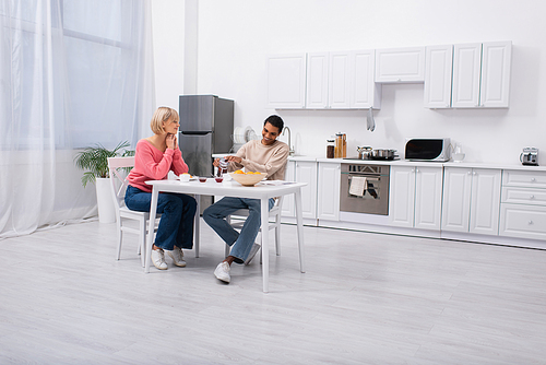 joyful african american man pouring tea near blonde girlfriend