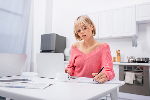 young woman writing on notebook near gadgets