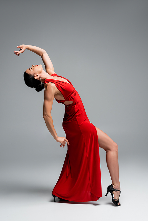 Side view of professional ballroom dancer in red dress moving on grey background