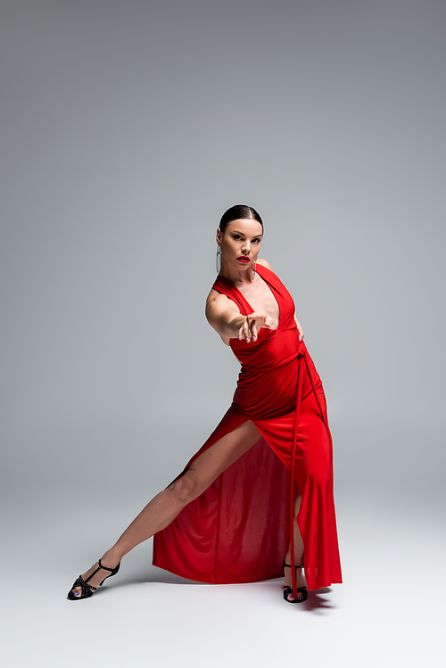 Full length of ballroom dancer in red dress looking at camera on grey background