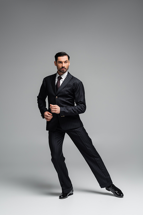 Full length of ballroom dancer in suit moving on grey background